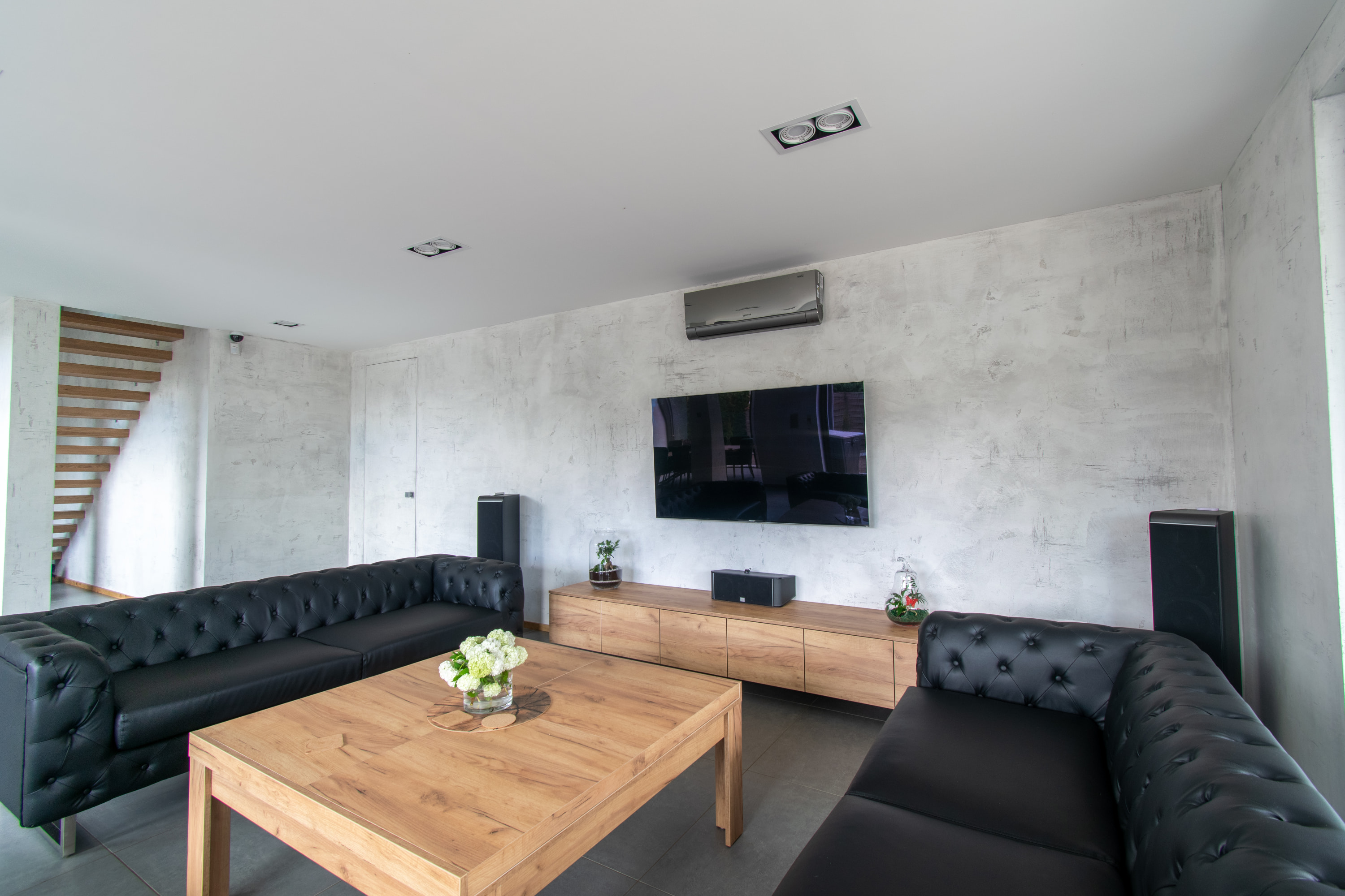 Salon z drapanym tynkiem Archi+Concrete na ścianach. Ukryte biuro w tle.